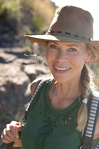 Mujer en primer plano sonriendo a la camara, con rocas montañosas de fondo.