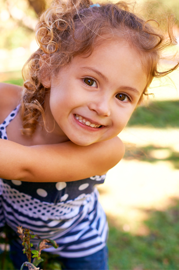 Niña en primer plano sonriendo a la camara, con un parque de fondo.